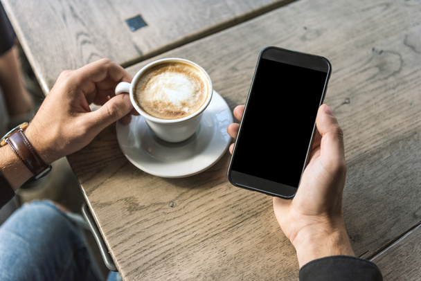 Oříznout záběr člověka s šálek cappuccino pomocí smartphone s prázdnou obrazovkou - Fotografie, Obrázek