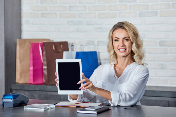beautiful young woman holding digital tablet with blank screen and smiling at camera while working in store   - Zdjęcie, obraz