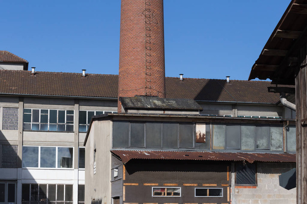 on a very sunny day in june in south germany you see elder architecture of an disused industrial zone with chimney and crashed windows and facades in need of renovation - Fotó, kép