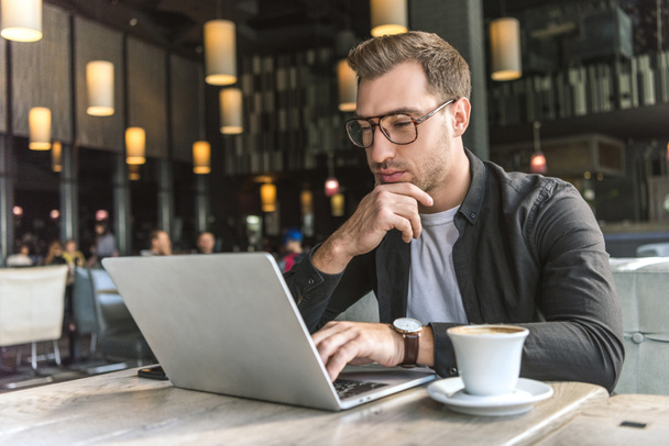 knappe jonge freelancer werken met laptop in café met een kopje koffie op tafel - Foto, afbeelding