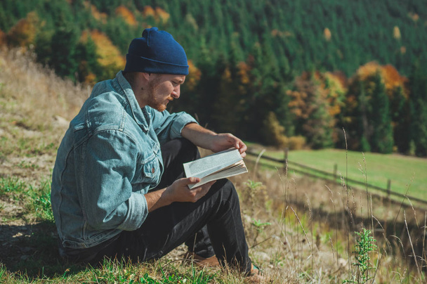 Young Man Traveler reading book, outdoor mountains on background Summer vacations and Lifestyle concept - Foto, afbeelding