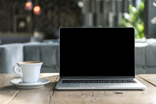 cup of delicious coffee and laptop with blank screen on rustic wooden table at cafe - Fotoğraf, Görsel