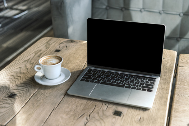 cup of cappuccino and laptop with blank screen on rustic wooden table at cafe - Foto, immagini