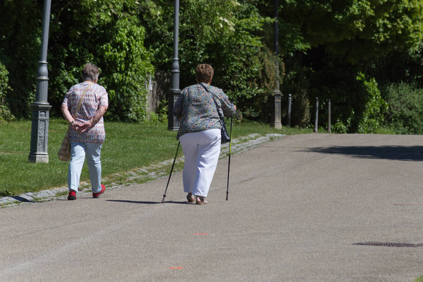 an einem sonnigen Junitag in Süddeutschland sieht man Seniorinnen und Senioren im Klosterpark auf einer Bank sitzen oder mit Nordic-Walking-Stöcken spazieren gehen - Foto, Bild