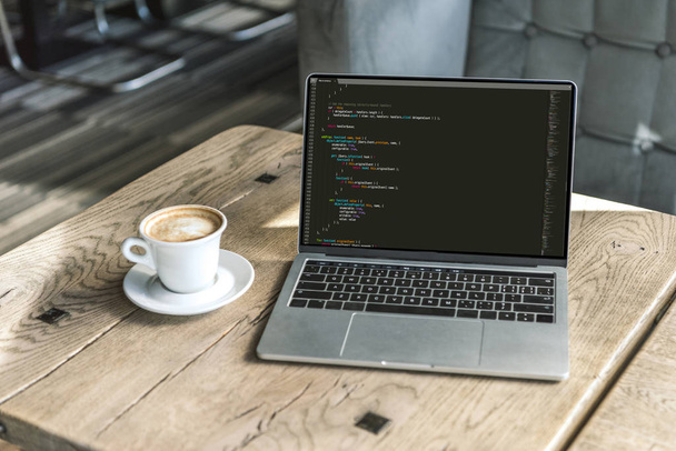 xícara de cappuccino e laptop com código de programa na tela na mesa de madeira rústica no café
 - Foto, Imagem