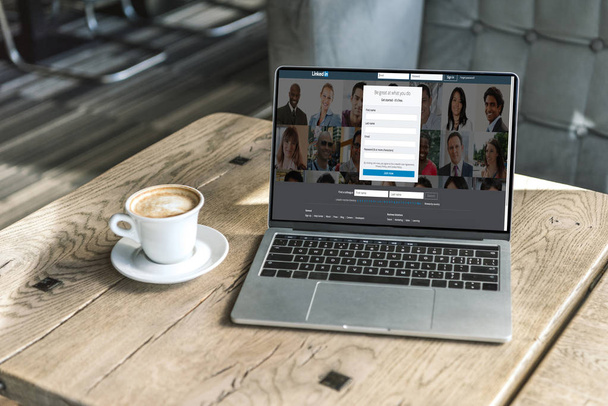 cup of coffee and laptop with linkedin website on screen on rustic wooden table at cafe - Fotoğraf, Görsel