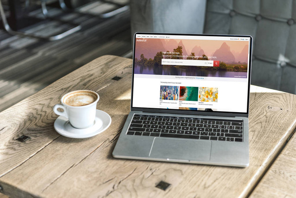 filiżankę kawy i laptopa z internetowej shutterstock na ekranie na drewnianym stole w kawiarni - Zdjęcie, obraz