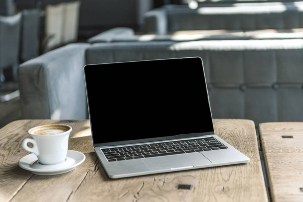 cup of coffee and laptop with blank screen on rustic wooden table at cafe - Foto, imagen