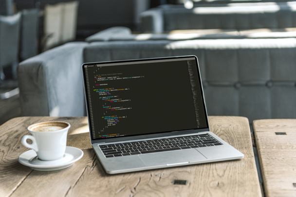xícara de café e laptop com código de programa na tela na mesa de madeira rústica no café
 - Foto, Imagem