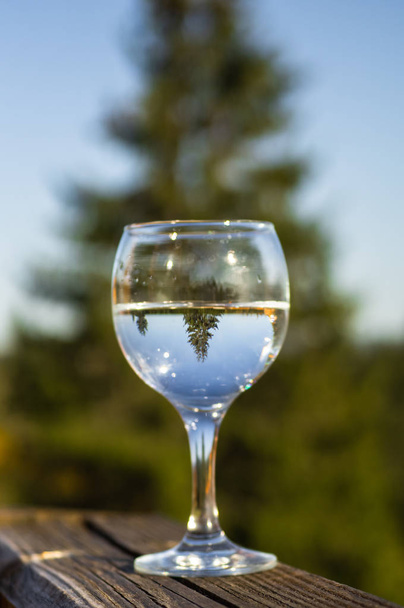 Egy pohár vízzel a hegyekre néző erkély. Tükör bemutatás egy pohár. Tűlevelű fa jelennek meg egy pohár - Fotó, kép