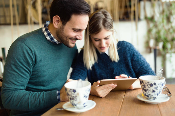 Young attractive couple using digital tablet in coffee shop - Фото, изображение