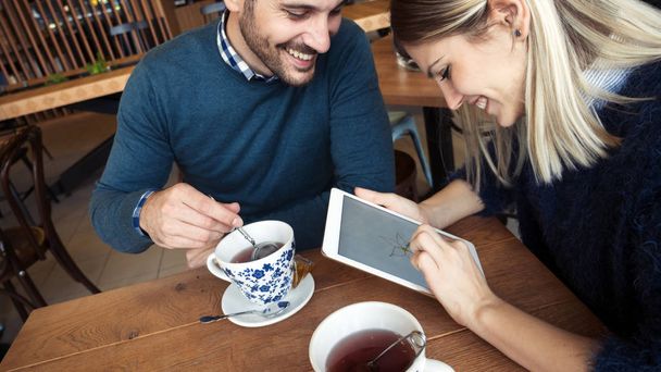 Young attractive couple using digital tablet in coffee shop - Фото, изображение