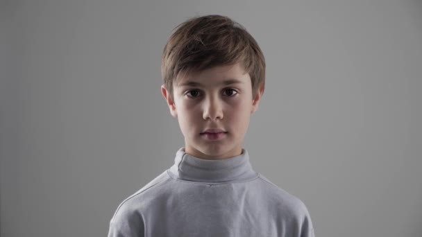 Portrait of cute young 11 - 12 year old boy looking at the camera on white background - Footage, Video
