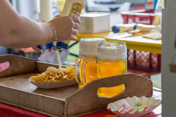 op buiten Tuinfeestje worden heerlijke frietjes geserveerd met server van rode ketchup en mayonaise op een rode tafel samen met glas Duits bier - Foto, afbeelding