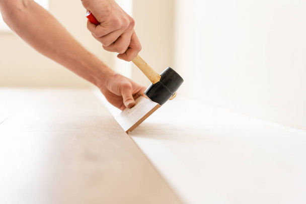 Strikes with a soft hammer on the part with a lock, for fixing. Installing laminate flooring fitting the next piece - focus on hand. Man laying laminate flooring - Zdjęcie, obraz
