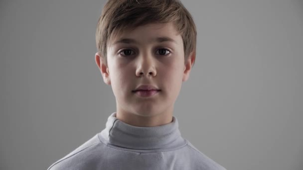 Portret cute młodych 11-12 roku chłopiec ogląda aparat na białym tle - Materiał filmowy, wideo