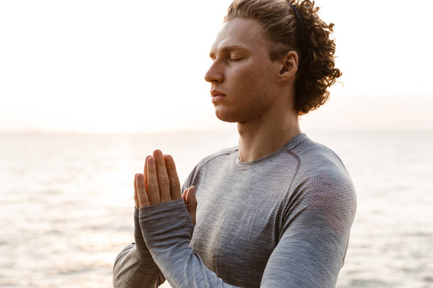 Image of handsome young sports man on the beach meditate outdoors. - Photo, Image