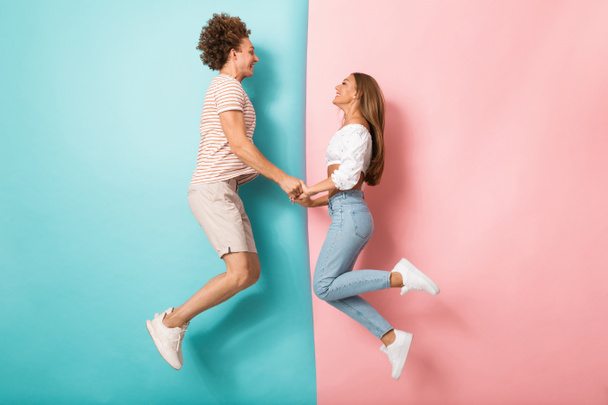 Full length portrait of a happy young couple jumping over two colored background, holding hands - Foto, Bild