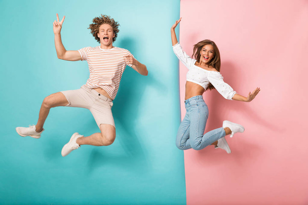 Full length portrait of a joyful young couple jumping over two colored background - Foto, imagen