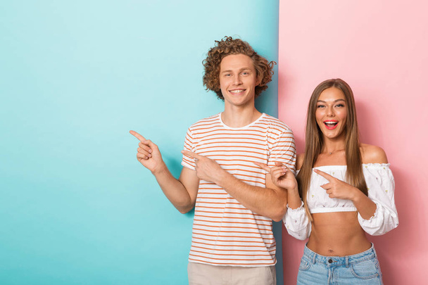 Portrait of a happy young couple standing over two colored background, pointing away - Foto, Bild