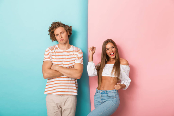 Portrait of a young couple standing over two colored background, woman is celebrating - Foto, Bild