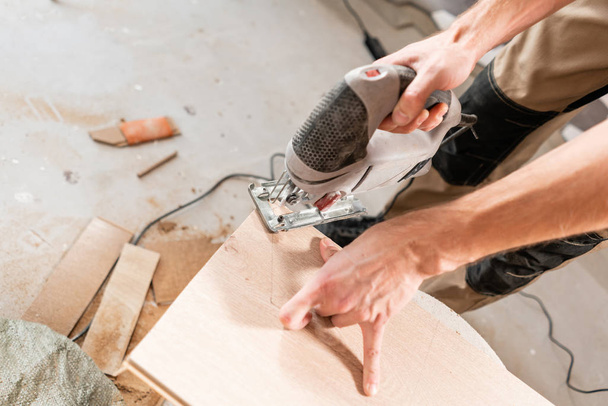 Ein männlicher Arbeiter schneidet die Laminatplatte mit einer Elektrolaubsäge. Verlegung neuer Holzlaminatböden. Konzept der Reparatur im Haus. - Foto, Bild