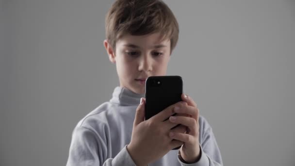 Portret młodych 11-12 roku chłopiec korzystanie ze smartfona na białym tle - Materiał filmowy, wideo