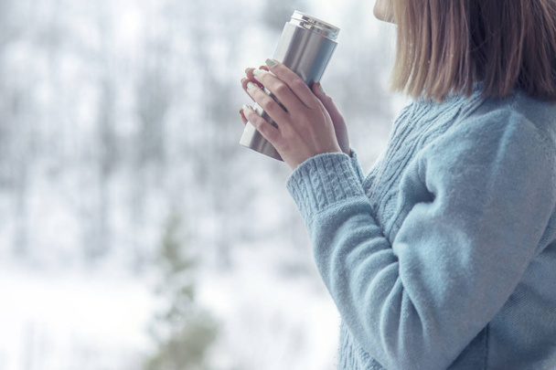 Woman in the background of a winter forest in a thermos bottle in hands - Photo, image