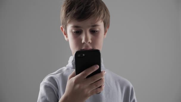 Portret młodych 11-12 roku chłopiec korzystanie ze smartfona na białym tle - Materiał filmowy, wideo