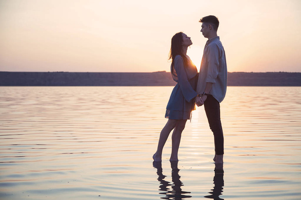 Любящая пара стоит на воде, держа за руки на фоне заходящего солнца
. - Фото, изображение
