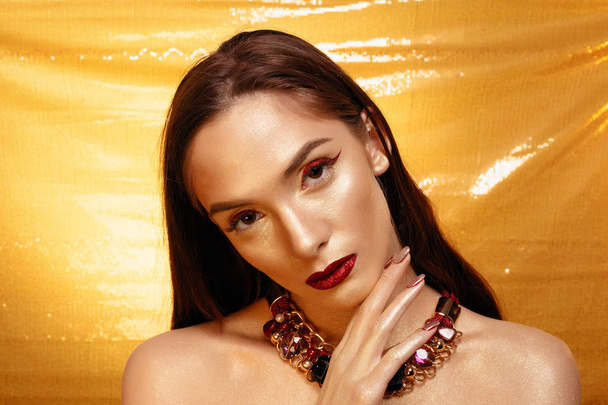 Magic Girl Portrait in Gold. Golden Makeup, close-up portrait in studio shot, color. Beauty Model Girl with perfect bright make-up, red lips, golden maroon jewellery. Sexy lady makeup Holiday party. - Zdjęcie, obraz