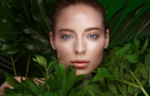 Beautiful fresh girl with perfect skin, natural make-up and green leaves. Beauty face. Photo taken in the studio. - Φωτογραφία, εικόνα