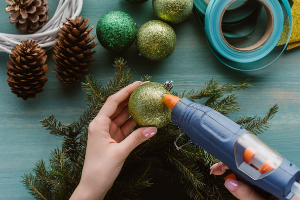 частковий вигляд жінки, що прикрашає сосновий вінок ручної роботи з різдвяними іграшками на синій дерев'яній поверхні
 - Фото, зображення