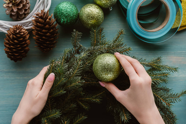 vista parcial de la mujer decorando la corona de pino hecha a mano con juguetes de Navidad en la superficie de madera azul
 - Foto, imagen