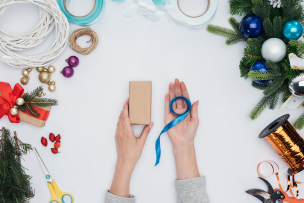vista parcial de la mujer sosteniendo cinta azul y regalo de Navidad envuelto en manos aisladas en blanco
 - Foto, Imagen