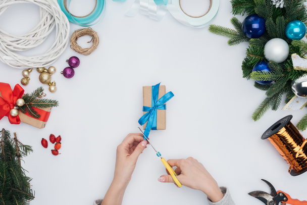 partial view of woman cutting blue ribbon on wrapped christmas present isolated on white - Fotografie, Obrázek