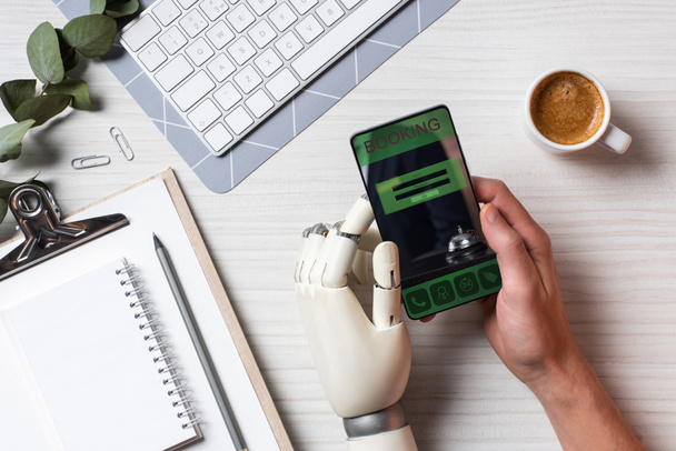 обрізане зображення бізнесмена з протезом рукою за допомогою смартфона з бронюванням на екрані за столом з чашкою кави в офісі
 - Фото, зображення