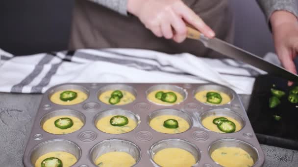 Cropped view of female chef preparing cornbread cupcakes with jalapeno pepper in muffin pan - Footage, Video