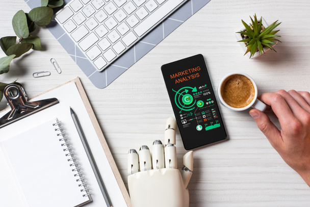 частковий вид на бізнесмена з протезом рукою за допомогою смартфона з маркетинговим аналізом на екрані за столом з чашкою кави в офісі
  - Фото, зображення