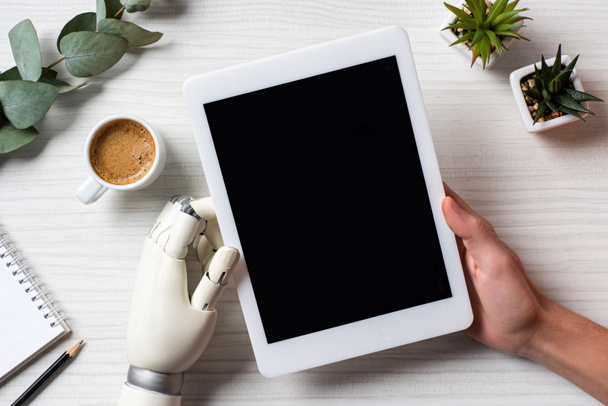 частичный взгляд бизнесмена с протезной рукой с помощью цифрового планшета с чистым экраном за столом с чашкой кофе в офисе
  - Фото, изображение
