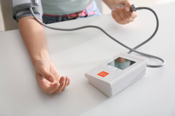 Mujer midiendo presión arterial con esfigmomanómetro sobre mesa blanca
 - Foto, imagen