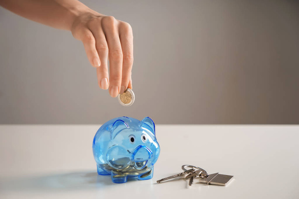Woman putting coin into piggy bank and keys on table. Concept of saving money for buying new house - Photo, Image