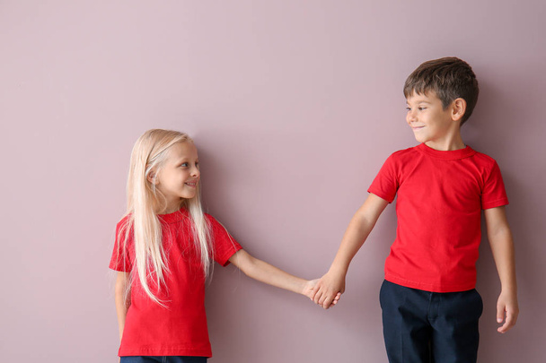 Мальчик и девочка в футболках держатся за руки на цветном фоне
 - Фото, изображение