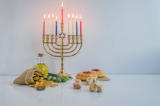 Jewish holiday hanukkah celebration with menorah (traditional candelabra), wooden dreidels (spinning top), donut, olive oil and chocolate coins on white table. table. table. - Photo, Image