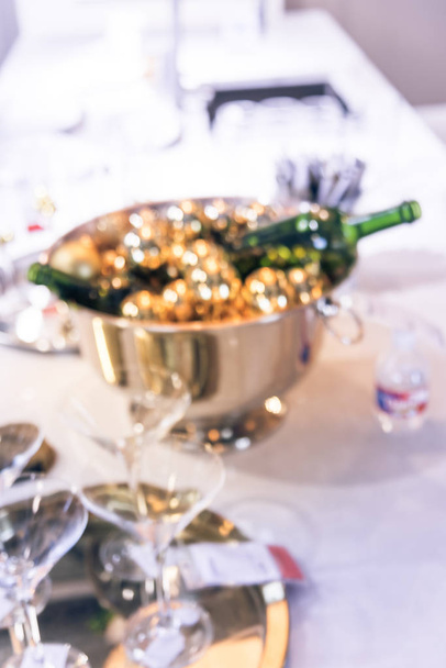 Beeld wazig vakantie setup tabelachtergrond. Mooie schone eettafel setting met champagne fles in de emmer, glazen en decoraties - Foto, afbeelding