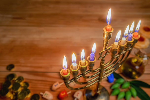 本枝の燭台 (伝統的な燭台)、木製 dreidels (こま)、ドーナツ、オリーブ オイルと木製のテーブルの上のチョコレートのコインでユダヤ人の祝日のハヌカのお祝い. - 写真・画像