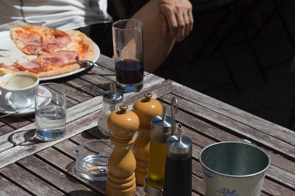 an einem sehr sonnigen Junitag in Süddeutschland sehen Sie ein Gartenrestaurant mit Pärchen, das in einem von Bäumen umgebenen Kreuzgang mit Schinken-Pizza, grünem Salat und Kaffee zu Mittag isst - Foto, Bild