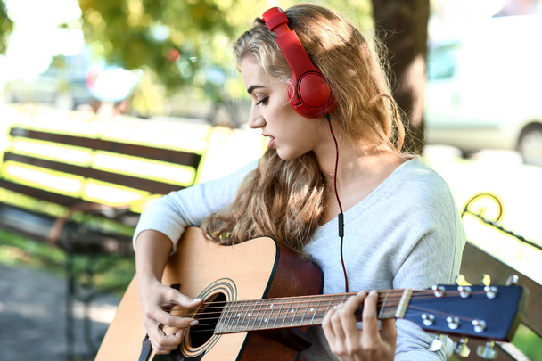 Piękna młoda kobieta, słuchanie muzyki i gra na gitarze w parku - Zdjęcie, obraz
