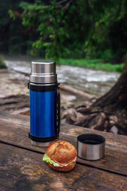 Bekijk op de blauw thermos op de houten tafel op de trekking parcours. Pauze voor warm drinken.  - Foto, afbeelding