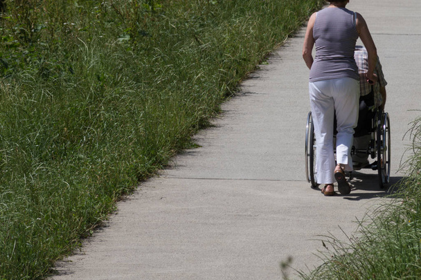 en un día muy soleado en junio en el sur de Alemania se ve a una mujer soltera empujando rollator en un paseo por el parque verde
 - Foto, imagen